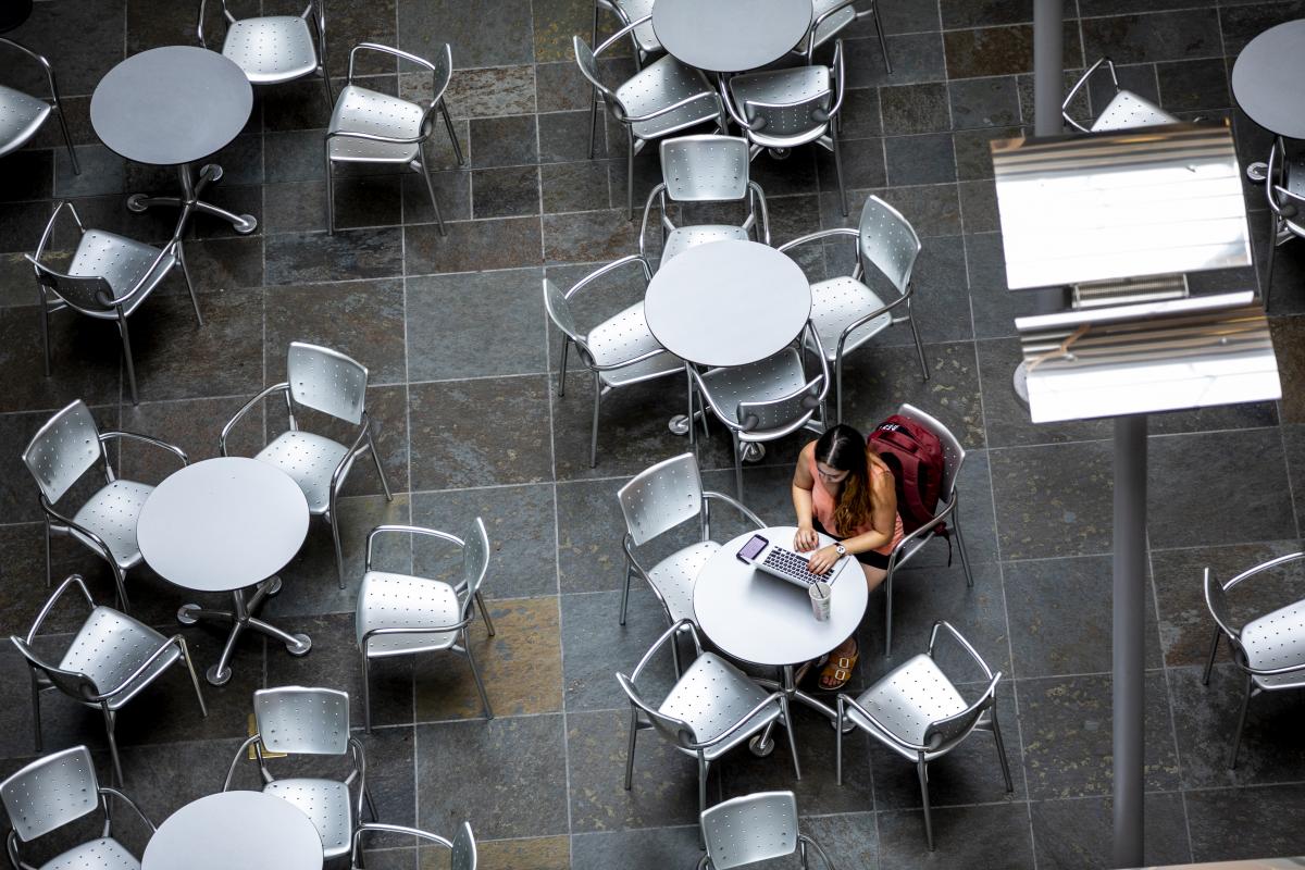 Rows of round cafe tables with four chairs from the Henry Art Gallery, one seat occupied by someone working on their computer