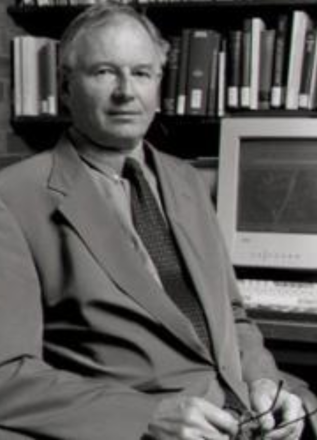 A black and white image of Eugene Vance sitting in front of a computer on a bookcase.