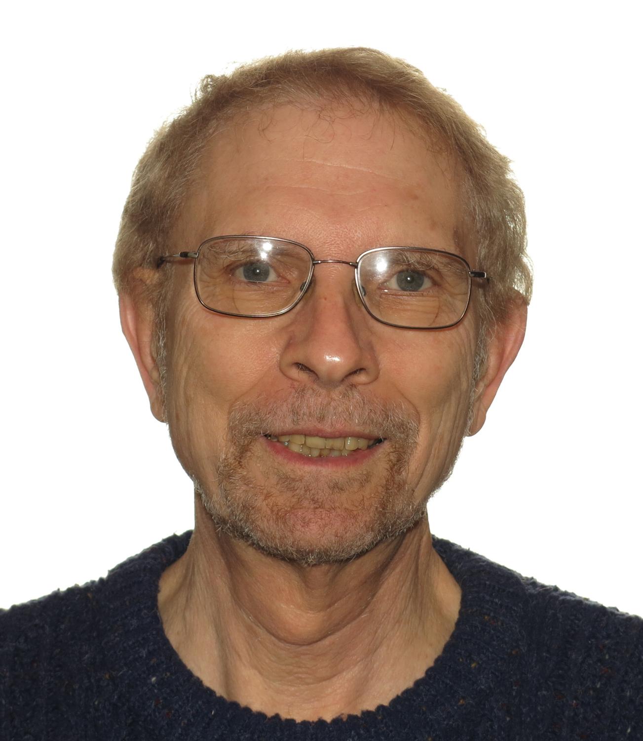 Frederick Newmeyer looks into the camera against a white background. He wears glasses and a black shirt.