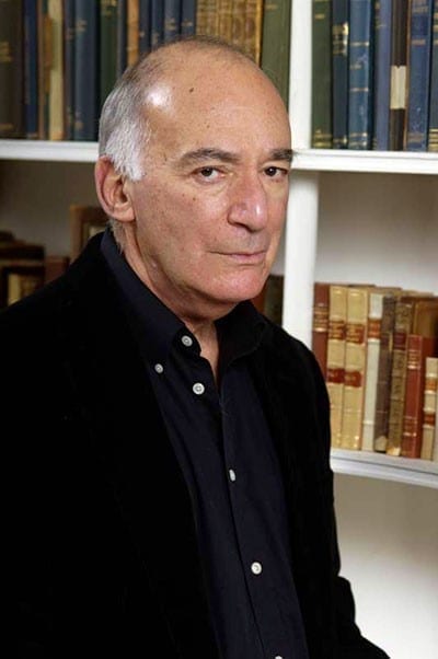 Michael Fried looks at the camera while standing in front of a bookcase.