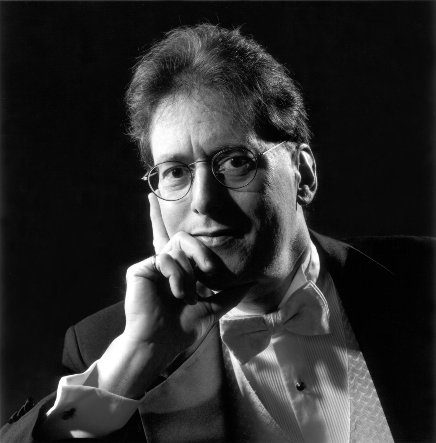 A black and white image of Robert Levin looking into the camera while leaning his head on his hand.