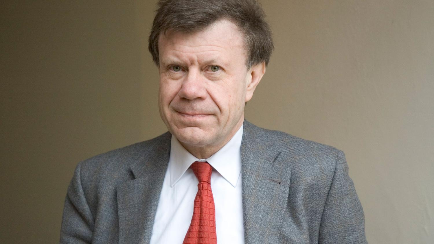 Roger Chartier looks into the camera while wearing a grey suit and red tie.