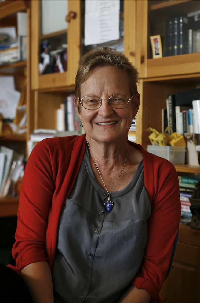 Heather McHugh looks into the camera while wearing a red cardigan and grey shirt.