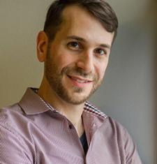 Abraham Avnisan stands in front of a white wall wearing a patterned shirt. 