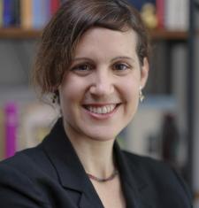 Mika Ahuvia in suit jacket smiling with bookcase in background 