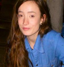 Annie Fee sits in front of a dark wall wearing a blue shirt.