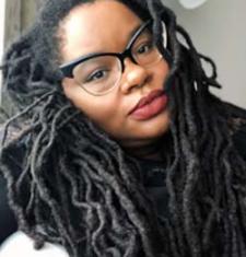 A close-up portrait of Bettina Judd wearing glasses and a dark shirt.