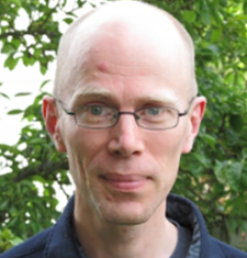 Portrait of Charles LaPorte wearing glasses and standing in front of a tree.