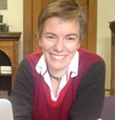 Cricket Keating sits behind a desk wearing a red and grey sweater.