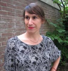 Jenna Grant stands outside in front of a brick wall wearing a patterned shirt. 