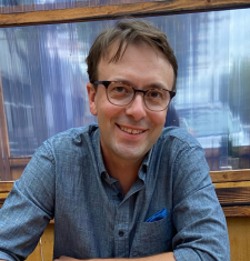 A close-up image of Jesse Oak Taylor wearing a blue shirt and glasses.