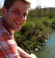 Justin Mohler looks at the camera while sitting in front of a river.