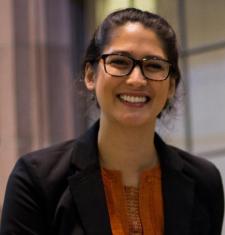 Profile of Katia smiling at the camera in a dark blazer and orange shirt