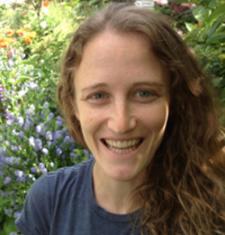 Lily Shapiro stands in front of a bush wearing a blue shirt.