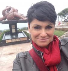 María Elena García stands outside wearing a red scarf and grey jacket.