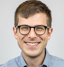 Matthew Bellinger stands in front of a white wall wearing a patterned shirt and glasses.