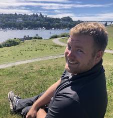 Matthew Childs sits outside on a hill overlooking a body of water.