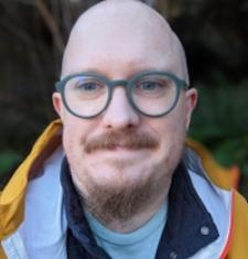 Matthew Poland looks at the camera while wearing green glasses.