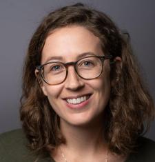 Headshot of Melanie Walsh standing in front of a grey wall wearing glasses.