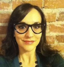 Pamela Pietrucci stands in front of a brick wall wearing glasses an a green shirt.