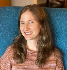 Adair Rounthwaite sits on a blue chair wearing a pink sweater. 