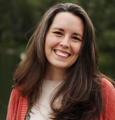 Sarah Moore stands outside while wearing a read cardigan and white shirt.