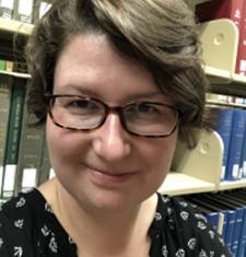 Verena Kick stands in front of a bookcase wearing glasses and a dark shirt.