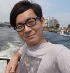 Yuta Kaminishi stands in front of a body of water wearing glasses and a grey shirt.