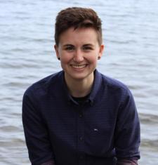 Profile picture of Sarah Brucia Breitenfeld: a person with short brown hair in a blue button up sitting in front of a lake.