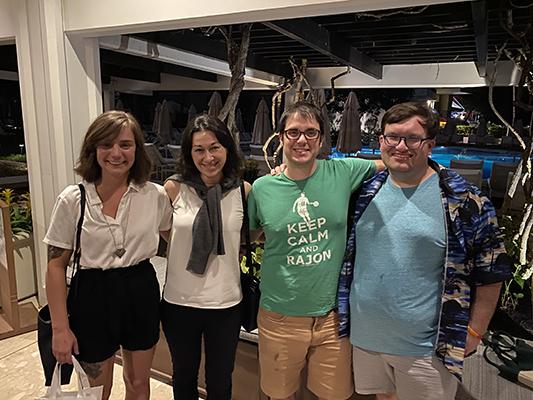 Four people stand arm in arm and smile into the camera.