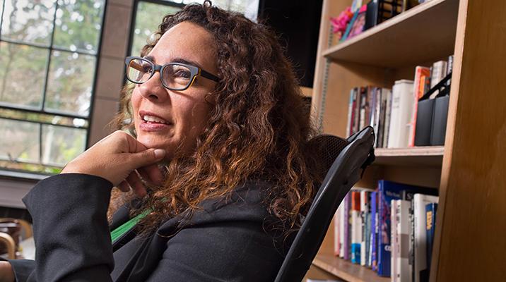 Ralina Joseph sits in front of a bookcase wearing glasses and a dark jacket.