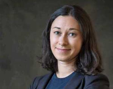 Rachel Arteaga looks into the camera wearing a blue shirt and dark blazer against a gray background.