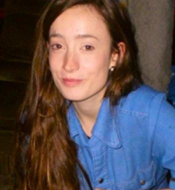 Annie Fee sits in front of a dark wall wearing a blue shirt.