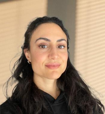 Photo of Gabrielle Benabdallah wearing a dark shirt and standing in front of a beige wall.