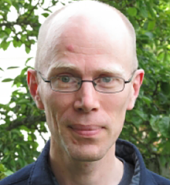 Portrait of Charles LaPorte wearing glasses and standing in front of a tree.