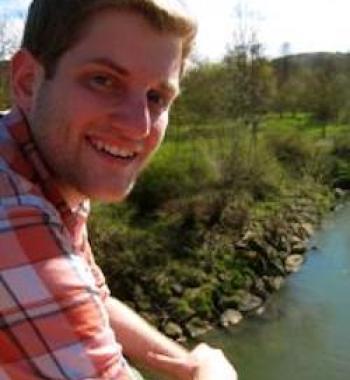 Justin Mohler looks at the camera while sitting in front of a river.