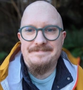 Matthew Poland looks at the camera while wearing green glasses.