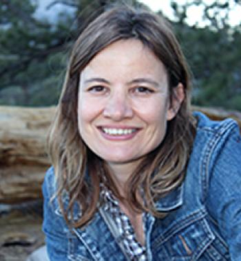 Minda Martin sits outside wearing a denim jacket and patterned shirt. 