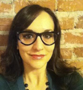 Pamela Pietrucci stands in front of a brick wall wearing glasses an a green shirt.