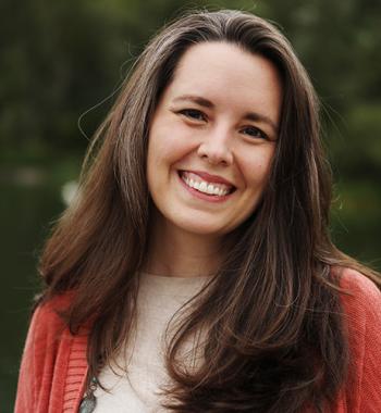 Sarah Moore stands outside while wearing a read cardigan and white shirt.