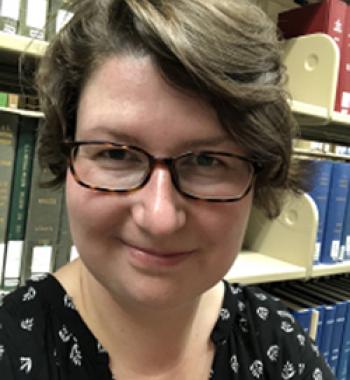 Verena Kick stands in front of a bookcase wearing glasses and a dark shirt.