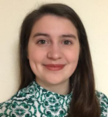 Close up of Hope smiling at the camera, long hair parted the side and in front of her right shoulder, behind her left shoulder. She is wearing a green patterned top and the backdrop is a cream color.