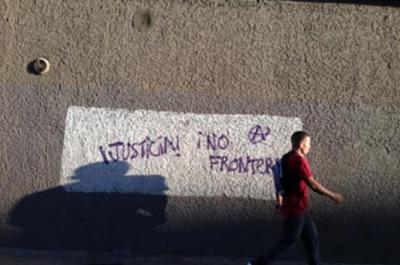 A man walks alongside a wall that has writing on it reading justice and no border in Spanish.