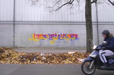 Image: "Unterwegs / On the Way" by Ella Ponizovsky Bergelson (2019, wall paint on concrete, Neukölln, Berlin). Part of a series of wall-writings created by Ella Ponizovsky Bergelson in 2018 and 2019 in many public places in Berlin. The multilingual text reads in German: 'Immer noch unterwegs', in Yiddish: 'נאך אונטערוועגן', and in Arabic: 'مازلت في الطريق', which translates into English: 'still on the way'.