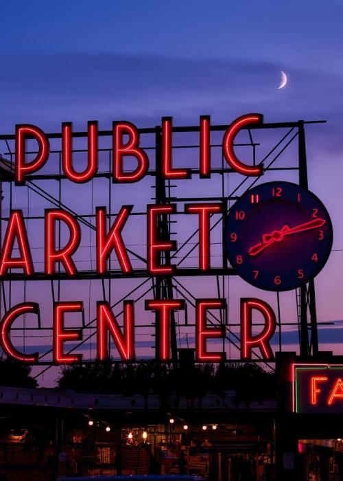 The signage for Pike Place Market illuminated against the sky at dusk.