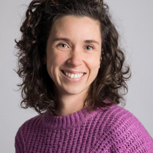 Audrey Desjardins stands in front of a white wall while wearing a lavender knit sweater.