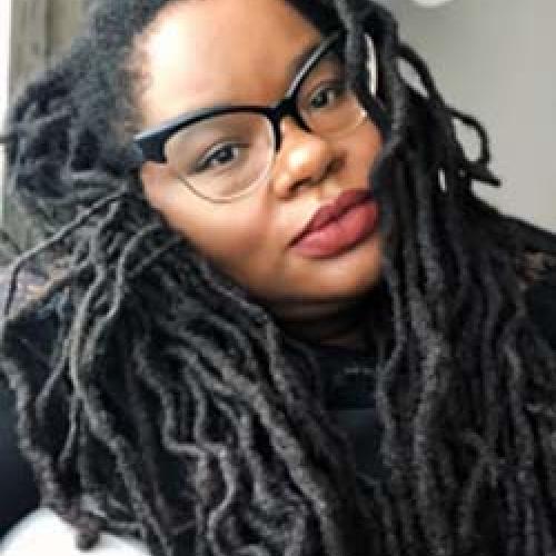 A close-up portrait of Bettina Judd wearing glasses and a dark shirt.