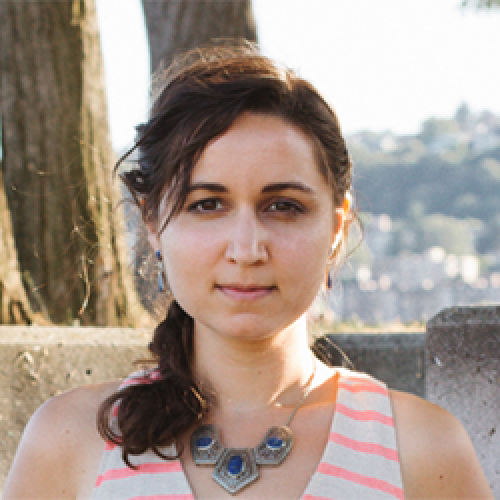 Anjuli Brekke stands in front of a tree and a landscape of houses while wearing a striped sleeveless top and a necklace.