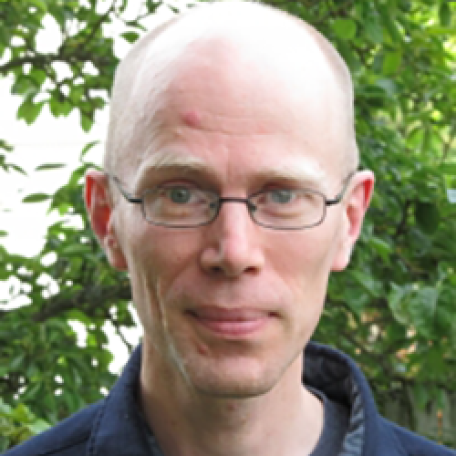 Portrait of Charles LaPorte wearing glasses and standing in front of a tree.