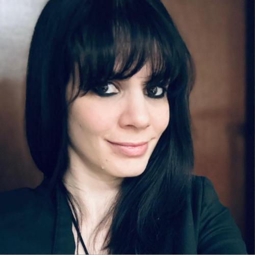 Melinda Cohoon looks into the camera while standing in front of a dark background.